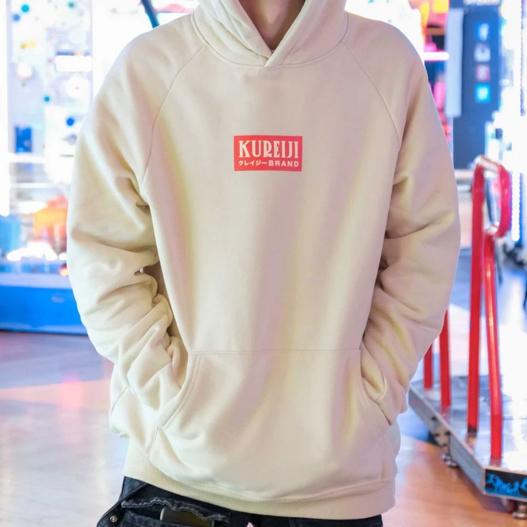 Person wearing a beige hoodie with 'KUREJI' branding in a blurred indoor setting